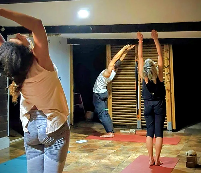 Élèves debout, les bras tendus vers le ciel, pendant un cours de yoga en salle