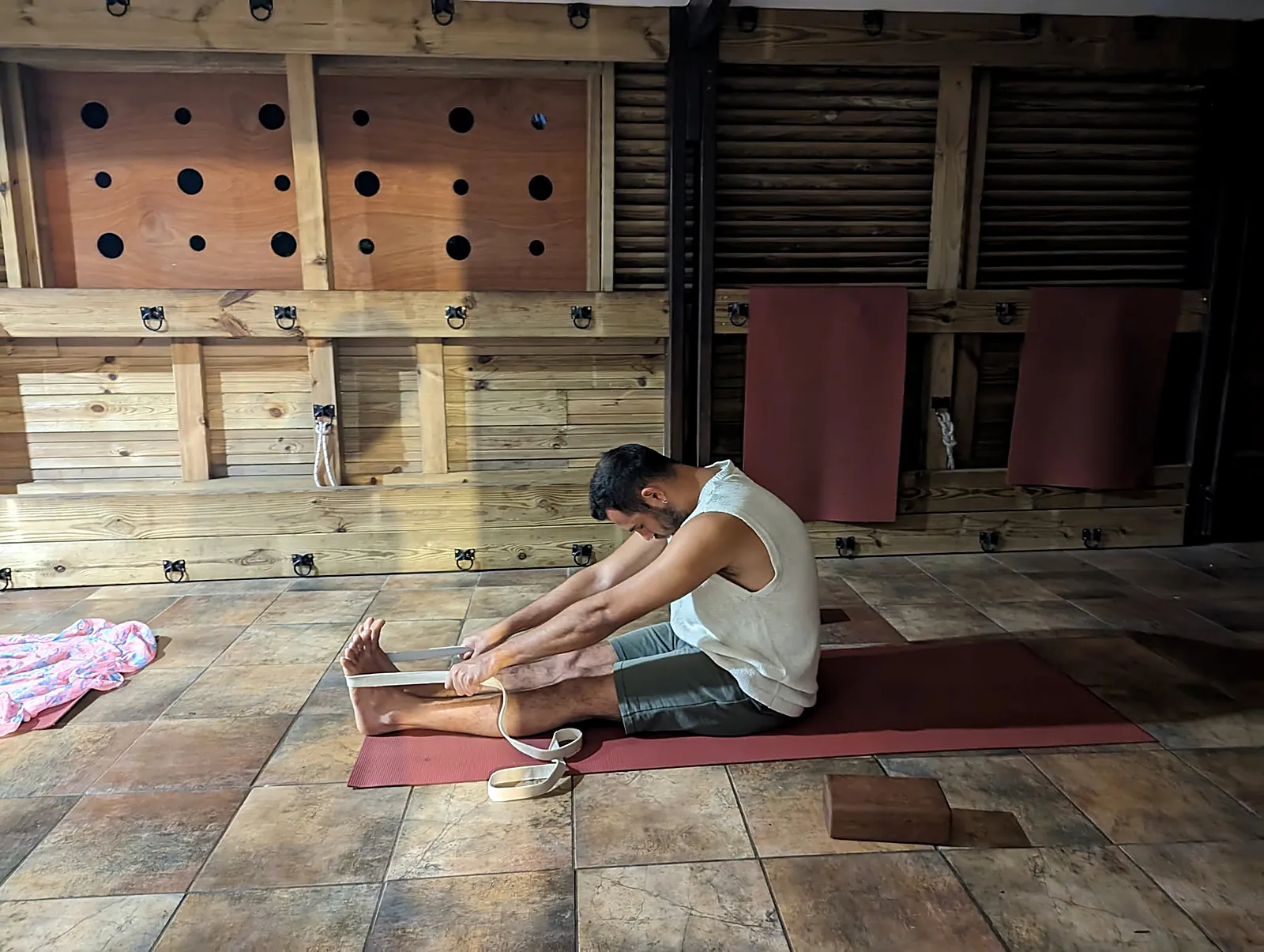 Élève assis en flexion avant, une sangle autour des pieds, pendant un cours de yoga en salle